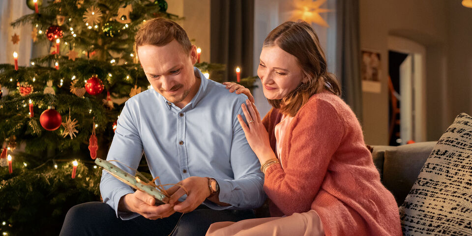 Couple sits on a couch looking at a photo book under a Christmas tree.