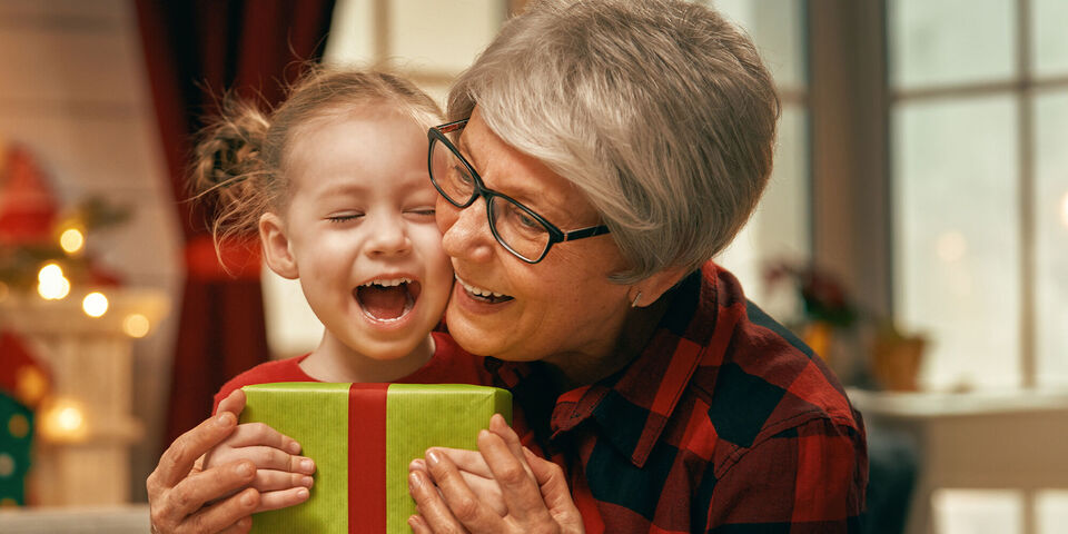 Grandparents hug a child while handing over a gift.