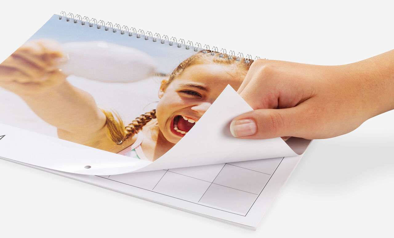 A hand flipping through a photo calendar, cheerful holiday pictures visible