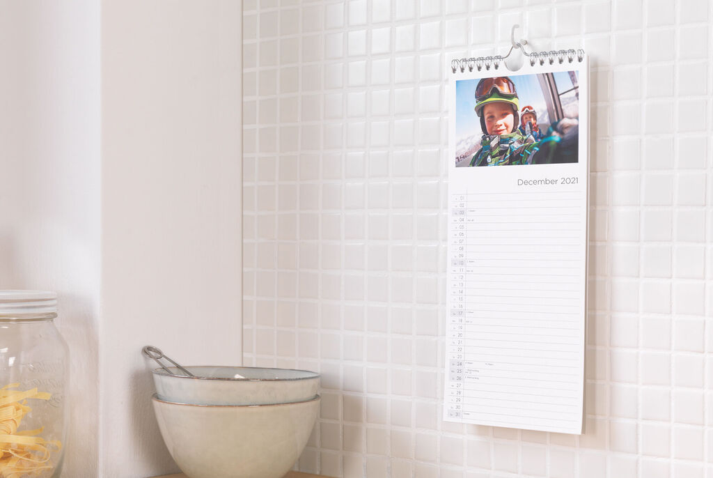 A wall calendar hangs on a bright wall. December 2023 visible, with a cheerful photo and note space.
