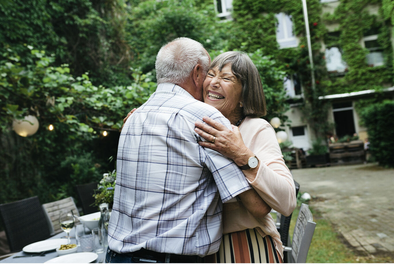 An older couple embraces lovingly in a beautiful garden. The atmosphere is warm and peaceful.