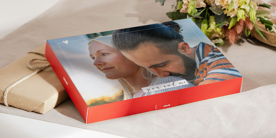 A lovingly designed CEWE photo book lies on a pretty table with a decorative background.