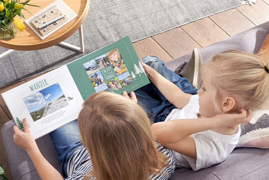 Two children sit on a sofa flipping through a CEWE photo book full of vacation photos, showing joy in discovering memories together.