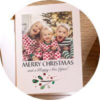 Two children in festive Christmas outfits laugh in front of a decorated tree