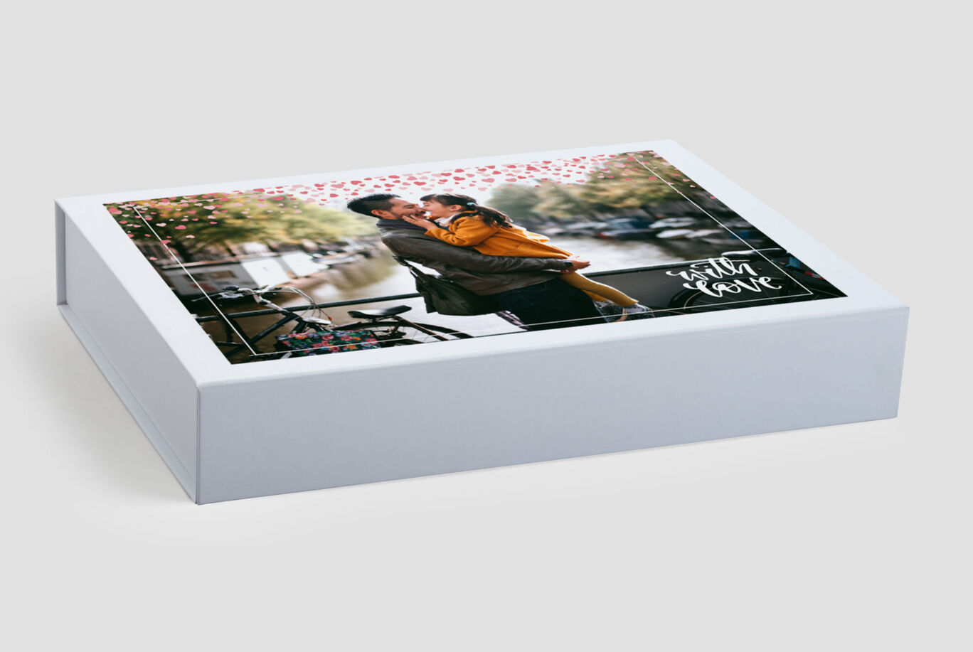 A loving couple embraces in front of a beautiful backdrop. The box shows their shared photo book.