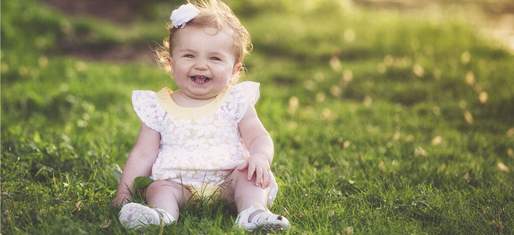 A small child sits happily on a green meadow enjoying a sunny day